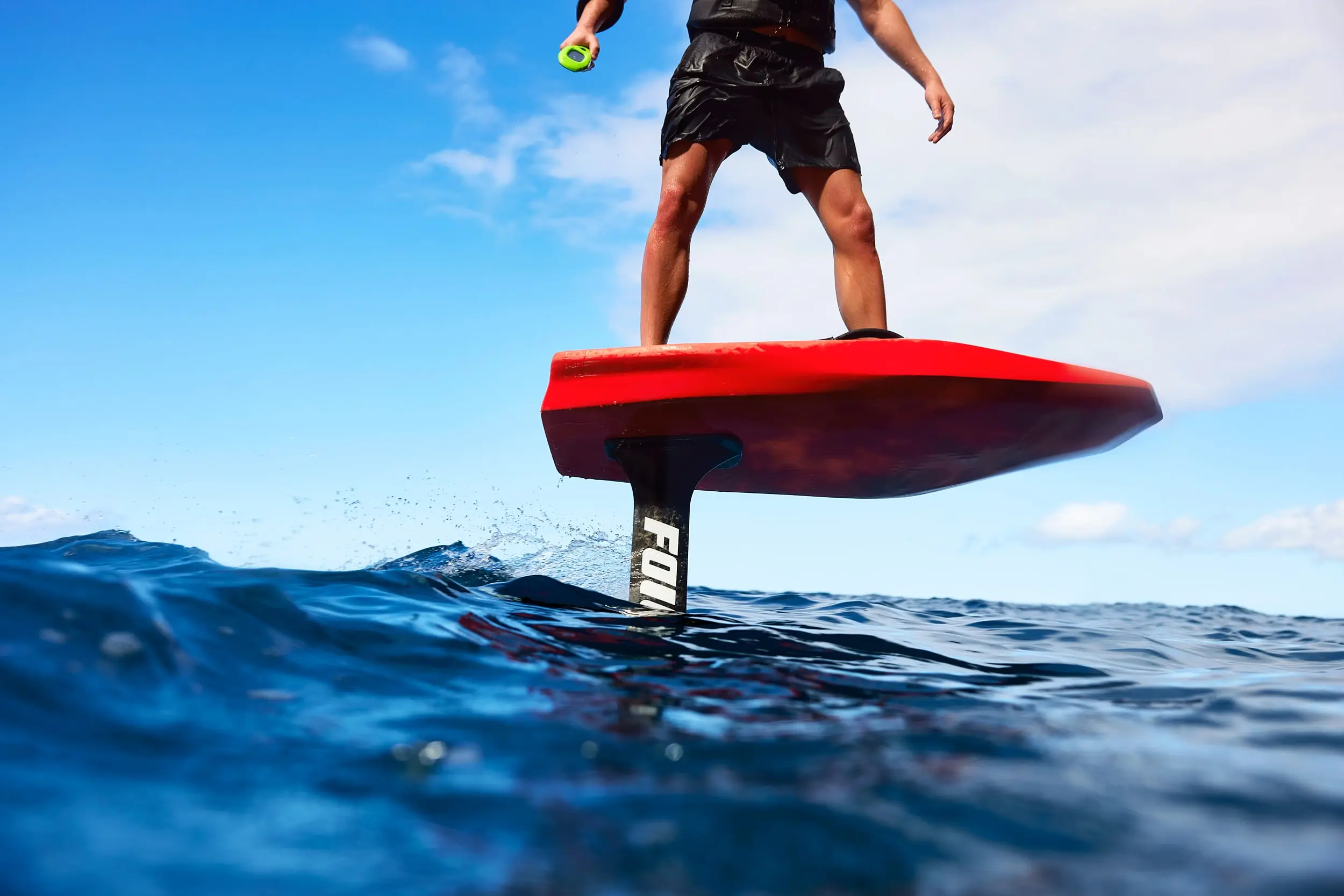 Waist-down shot of a male eFoil rider on a fuego-colored FOIL board. The board is carving through the water with clear blue skies in the background. 